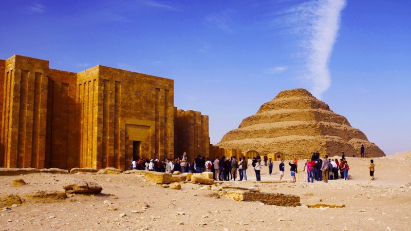 Tourists gather at the ancient Saqqara necropolis with the Step Pyramid in the background.