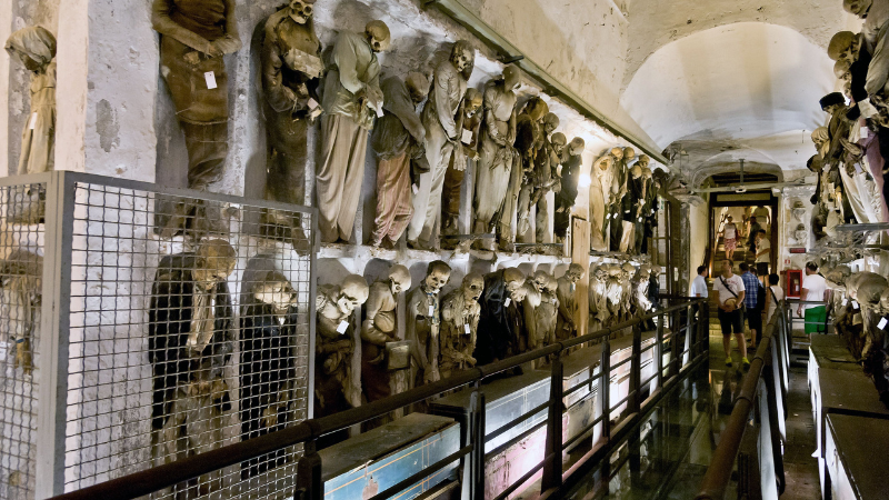 A catacomb with skeletal remains displayed along the walls.