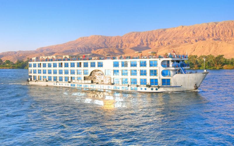 "A large river cruise ship with multiple decks sailing on the Nile River."