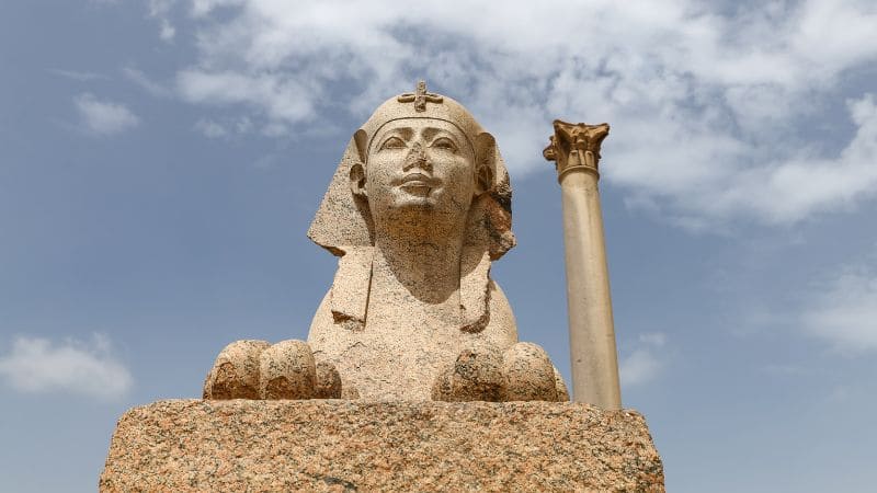 Sphinx statue and column against a clear sky.