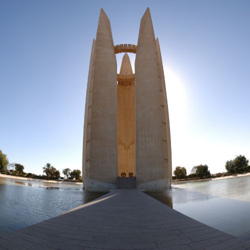 A symmetrical view of a towering monument with an arch at the top, flanked by water features under a clear sky.