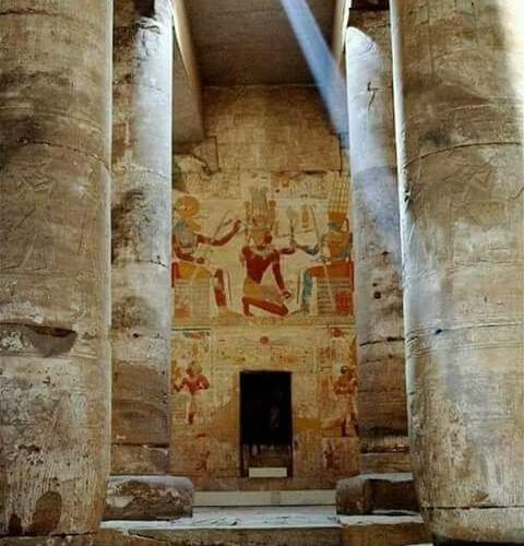 Shafts of sunlight illuminating the vibrant ancient hieroglyphs and carvings on the stone walls between large columns in an Egyptian temple