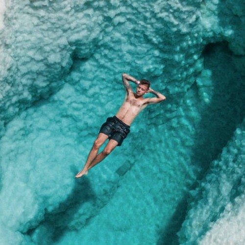 A person is floating on their back in crystal-clear blue waters