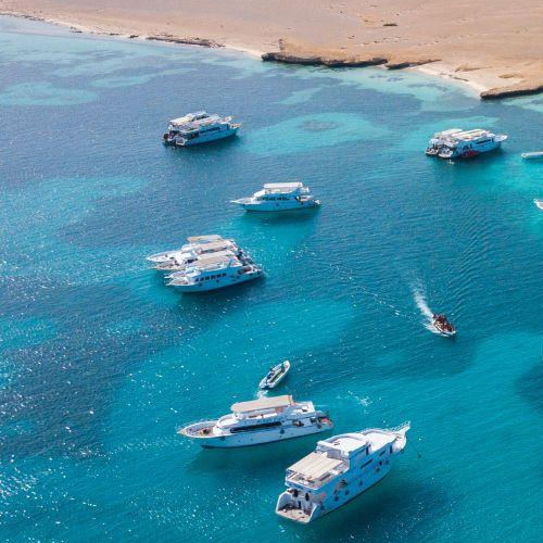 Aerial view of several boats and yachts on a clear blue sea near a sandy shore
