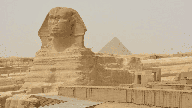 The Sphinx and a pyramid in the Giza complex under a hazy sky