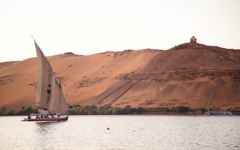 "Traditional felucca sailing on the Nile River with modern vessels in the background."