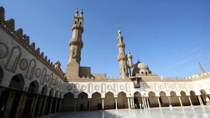 Wide courtyard of Al-Azhar Mosque in Cairo, featuring intricate architecture and towering minarets.