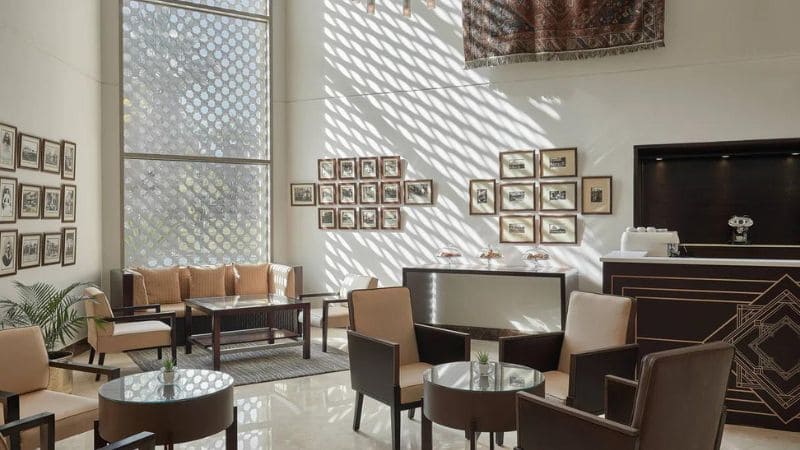 Modern hotel lobby with tall windows and patterned light casting shadows.