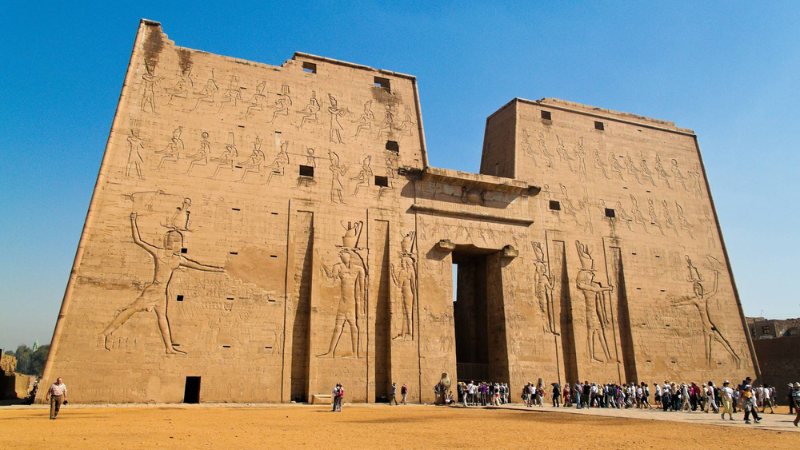 The massive entrance to an Egyptian temple, with crowds of visitors at its foot