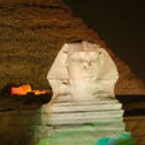 Illuminated Sphinx sculpture at night with a blurred pyramid in the background