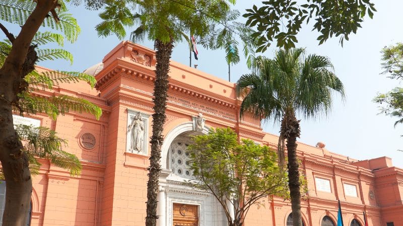 Facade of the Egyptian Museum in Cairo surrounded by palm trees.