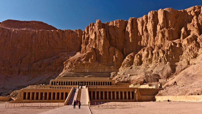 The imposing facade of the mortuary temple of Queen Hatshepsut with visitors approaching.