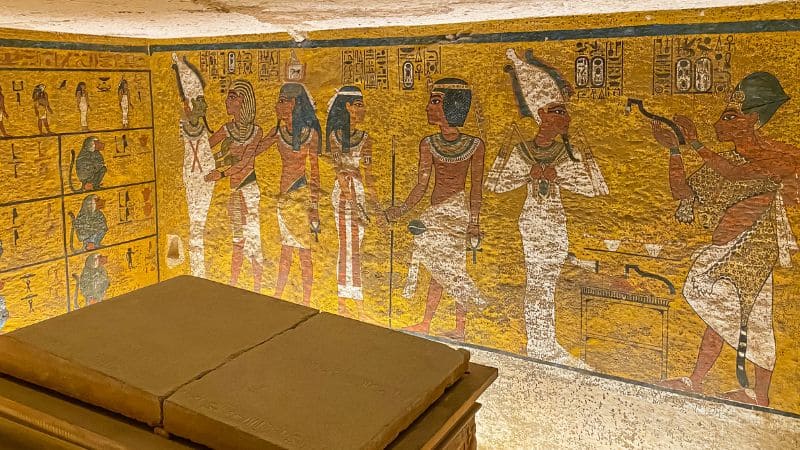 Colorful ancient Egyptian tomb paintings with hieroglyphs on a golden background.