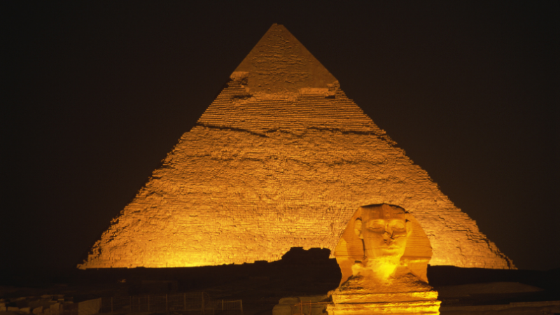 The Great Pyramid and Sphinx of Giza illuminated at night, casting a golden glow.