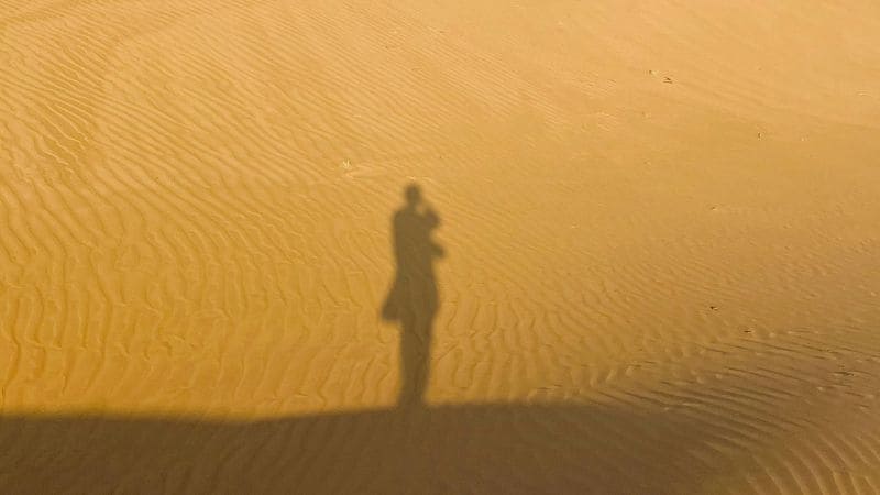 "Shadow of a person cast on rippled desert sands."