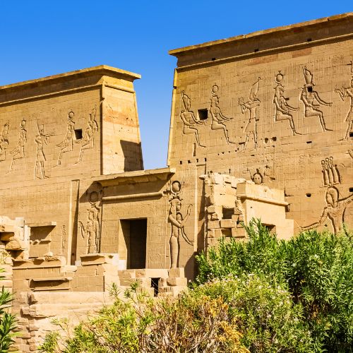 Ancient Egyptian temple with hieroglyphics and carvings of deities on its stone walls, under a clear blue sky.