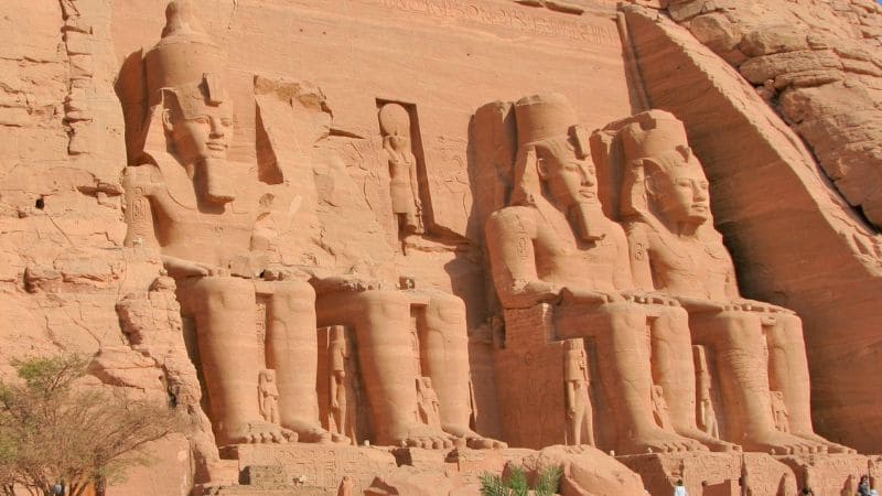 The colossal statues of Abu Simbel, carved into a rock cliff, standing under the bright sun.