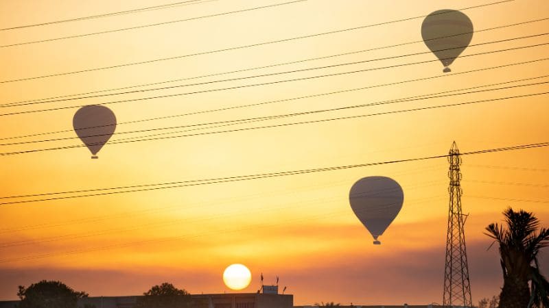 Hot air balloons soaring at sunrise near Luxor, Egypt, with power lines in the foreground.