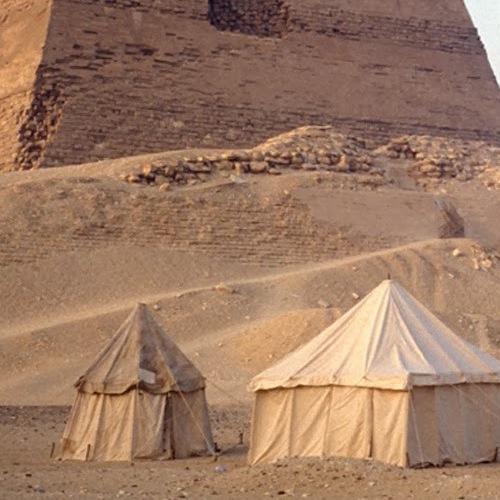 Two canvas tents set against the backdrop of a large pyramid in a desert.