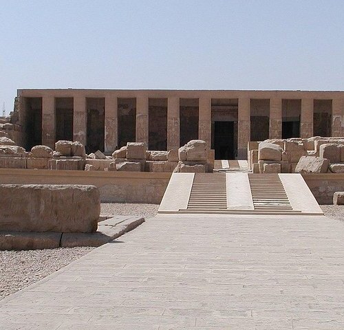 Front view of an ancient Egyptian temple with rows of columns and a clear blue sky
