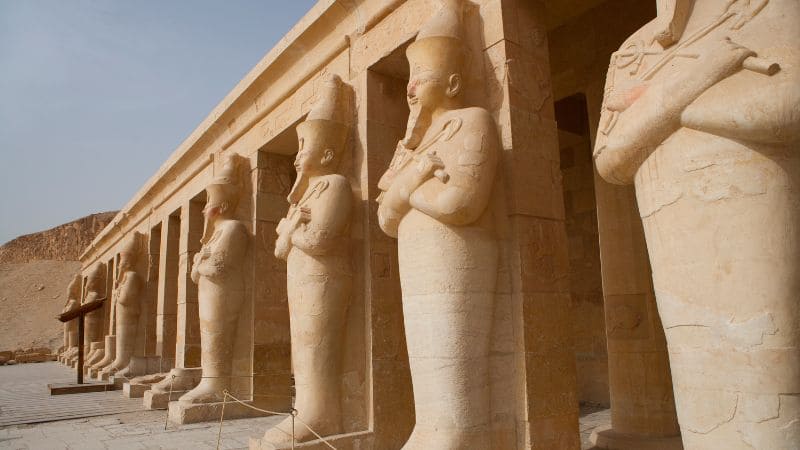 Colossal statues of a seated pharaoh outside a temple.