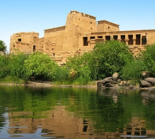 An ancient sandstone temple by a river, with its clear reflection on the water surface.