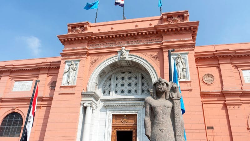 A historical building with a sculpture and flags under a blue sky.