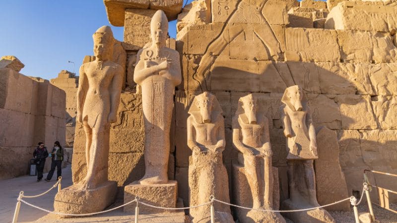 Stone statues stand in a row at Karnak Temple, with a clear sky above.