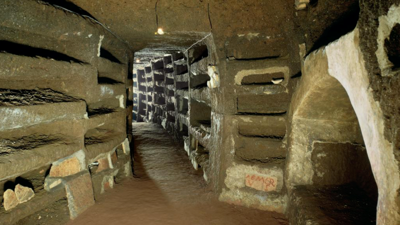 A narrow underground corridor with walls made of bricks, seen in dim lighting