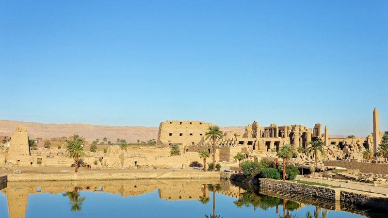 The ancient Karnak Temple complex reflected in a sacred lake under a clear sky.