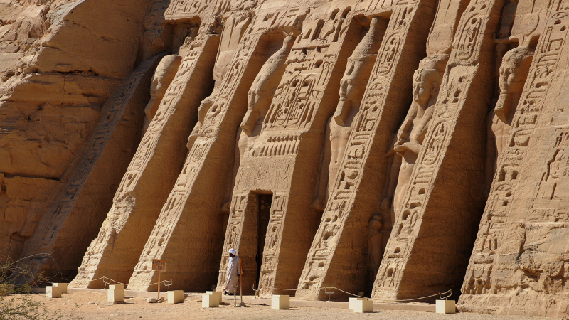 "A person stands dwarfed by the towering entrance of the temple at Abu Simbel."