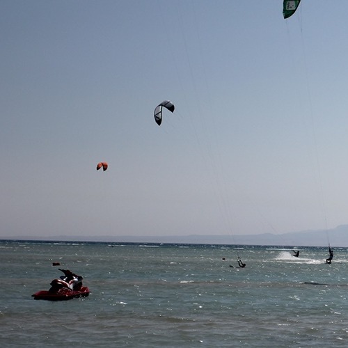 Kite surfers gliding on the sea under a clear sky with three colorful kites aloft