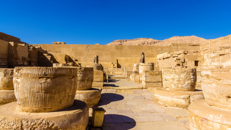 The ruins of Karnak Temple with ancient statues and columns under a clear blue sky.