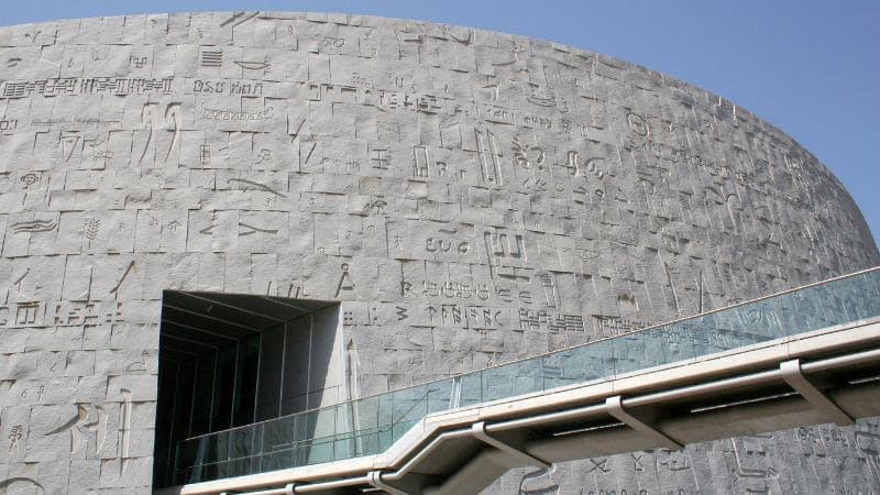 A modern building facade with inscriptions and hieroglyphics, under a blue sky.