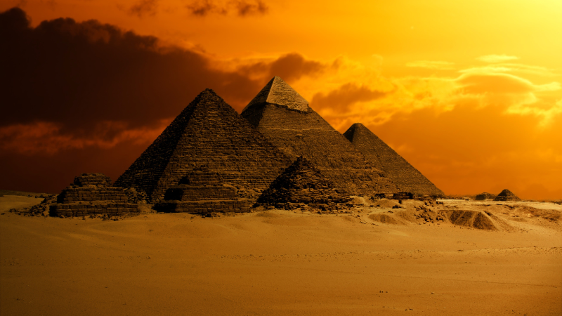 The Great Pyramids of Giza under a dramatic orange twilight sky