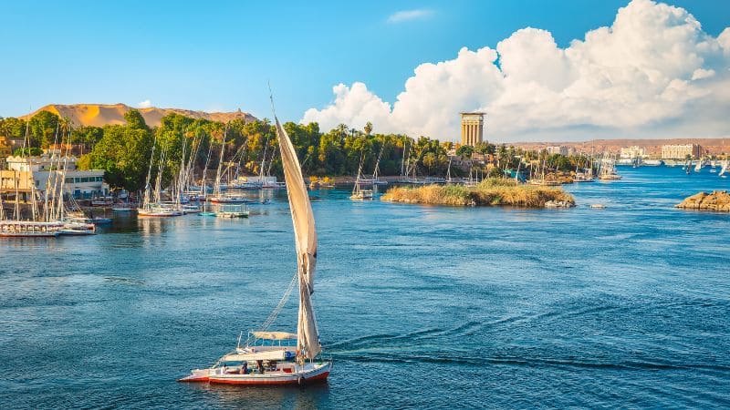 A traditional sailboat on the Nile River with a backdrop of blue skies and lush riverbanks.