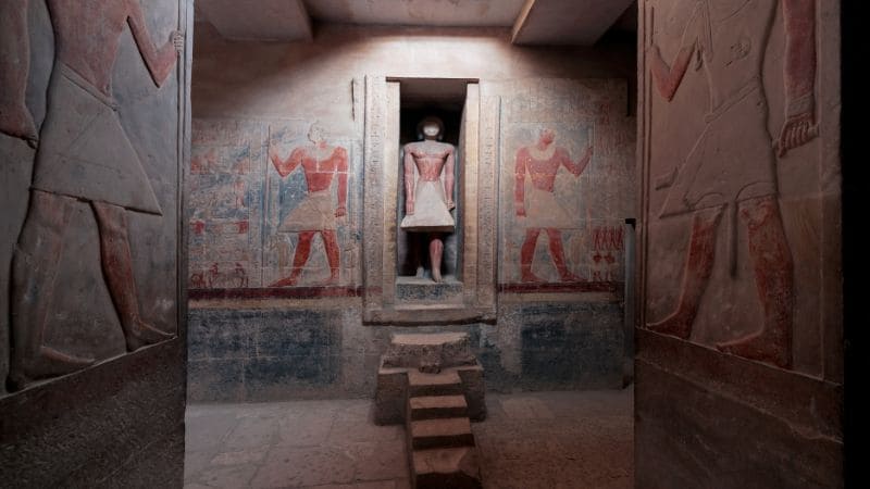 An ancient Egyptian tomb interior with vibrant hieroglyphics and a statue in a sanctuary.