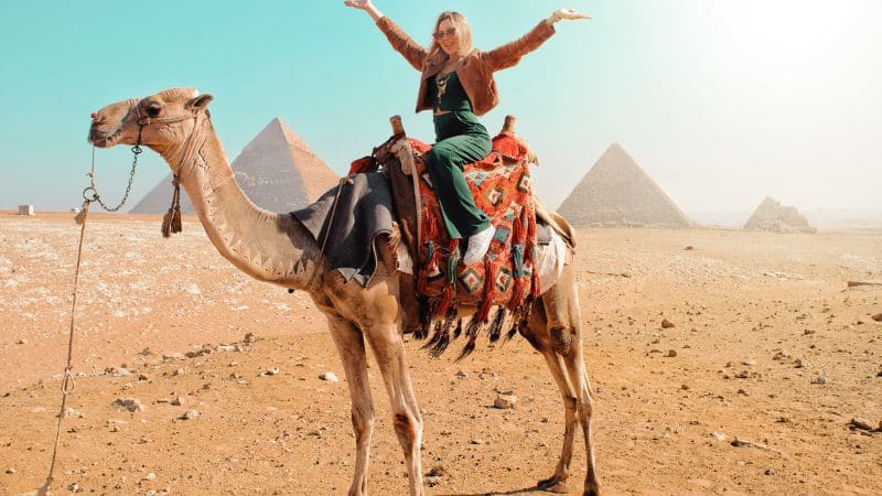 "Tourist on camel with Giza pyramids in the background."