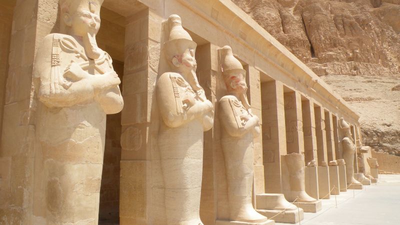 "Row of statues at the Temple of Hatshepsut against a mountain backdrop."