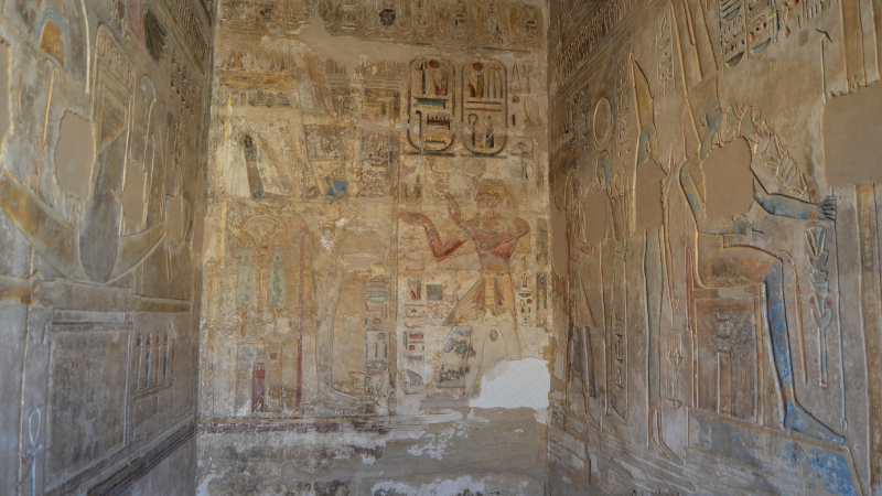 Faded frescoes depicting ancient Egyptian deities and symbols adorn a tomb chapel.