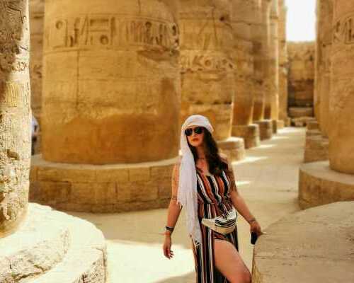 A woman in a striped jumpsuit poses amidst the ancient columns of an Egyptian temple.