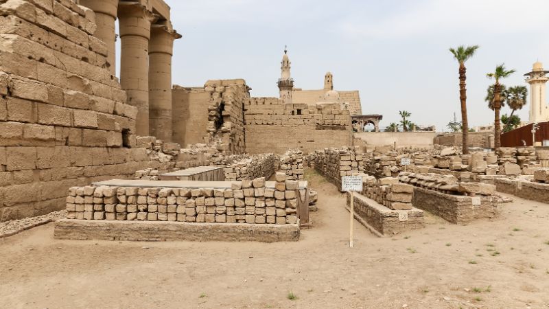 "Ruins of an ancient temple complex with a mosque in the background."