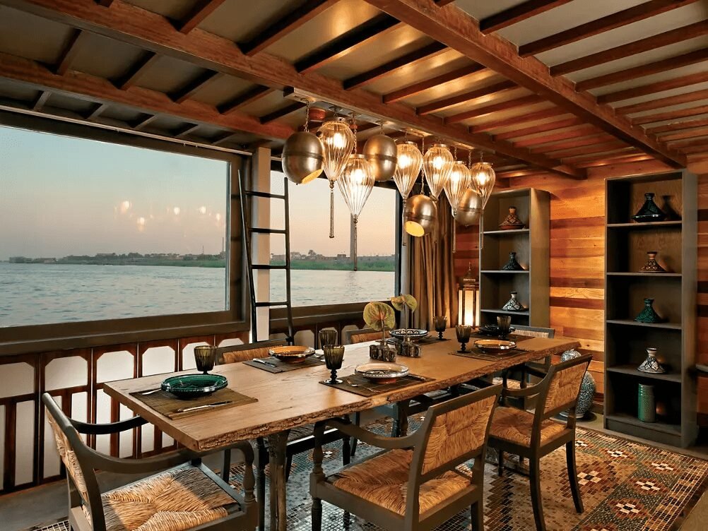Elegant outdoor dinner setup on board a luxury Dahabiya, with a table set under string lights and a clear starry sky