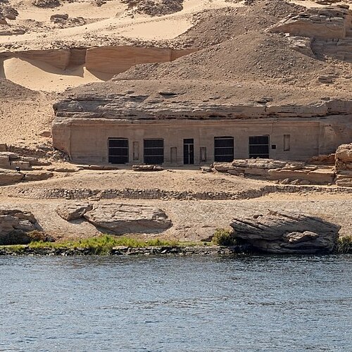 Ancient temple with rectangular doorways cut into a rock face along the Nile River