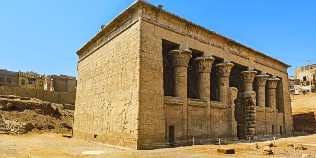 The side wall of the Esna Temple in Egypt with carved columns and hieroglyphs.