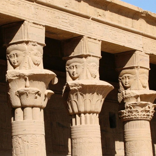 Ancient sandstone columns with carved faces of the goddess Hathor at the Temple of Esna in Egypt
