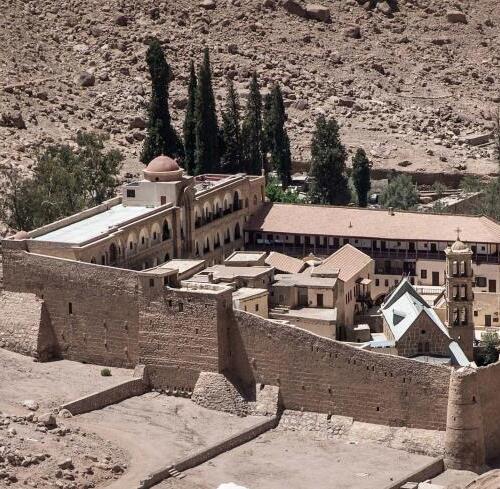 istoric monastery with terracotta roofs nestled among tall cypress trees in a barren desert landscape