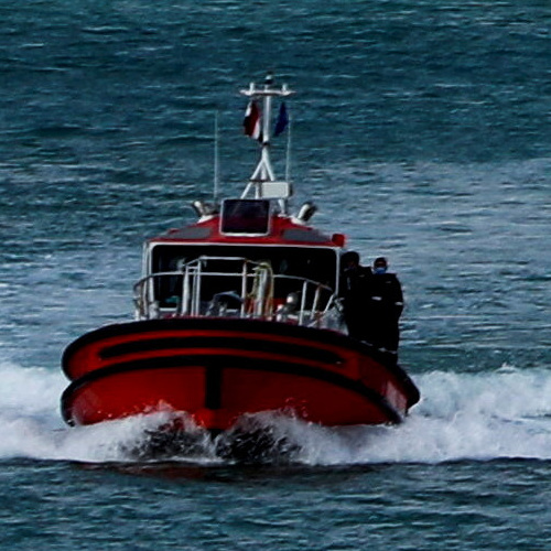 A red and black pilot boat cutting through blue waters