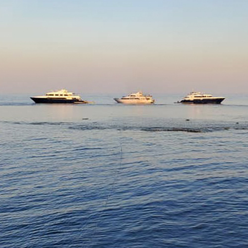 Three yachts floating on calm sea waters under a soft gradient sky at dusk