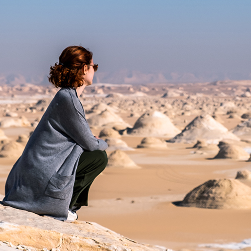 A woman sitting on a rock, gazing at the vast white desert landscape under a clear blue sky